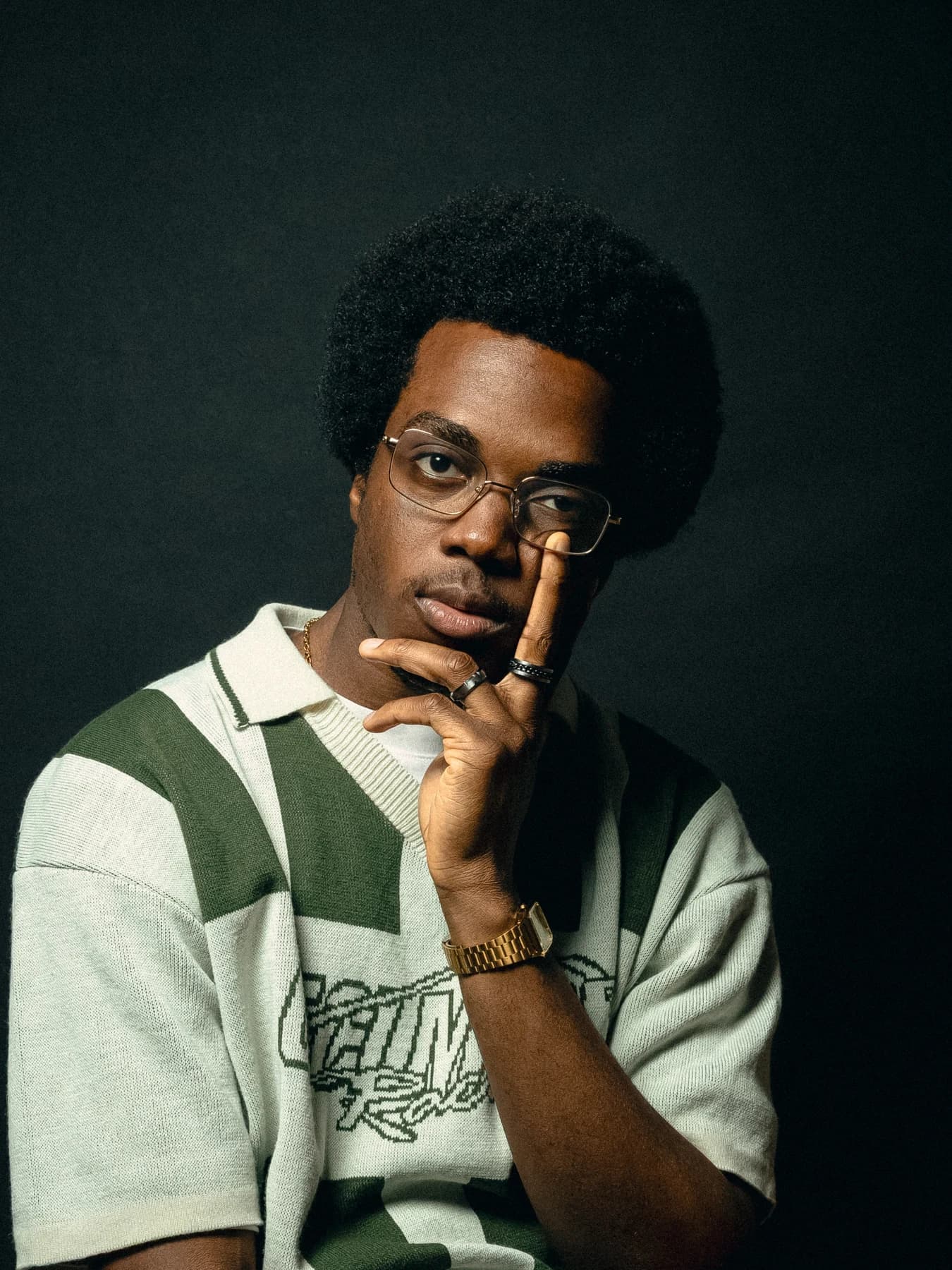 Portrait of Niyi Adeogun in a striped knit polo, resting his hand against his face