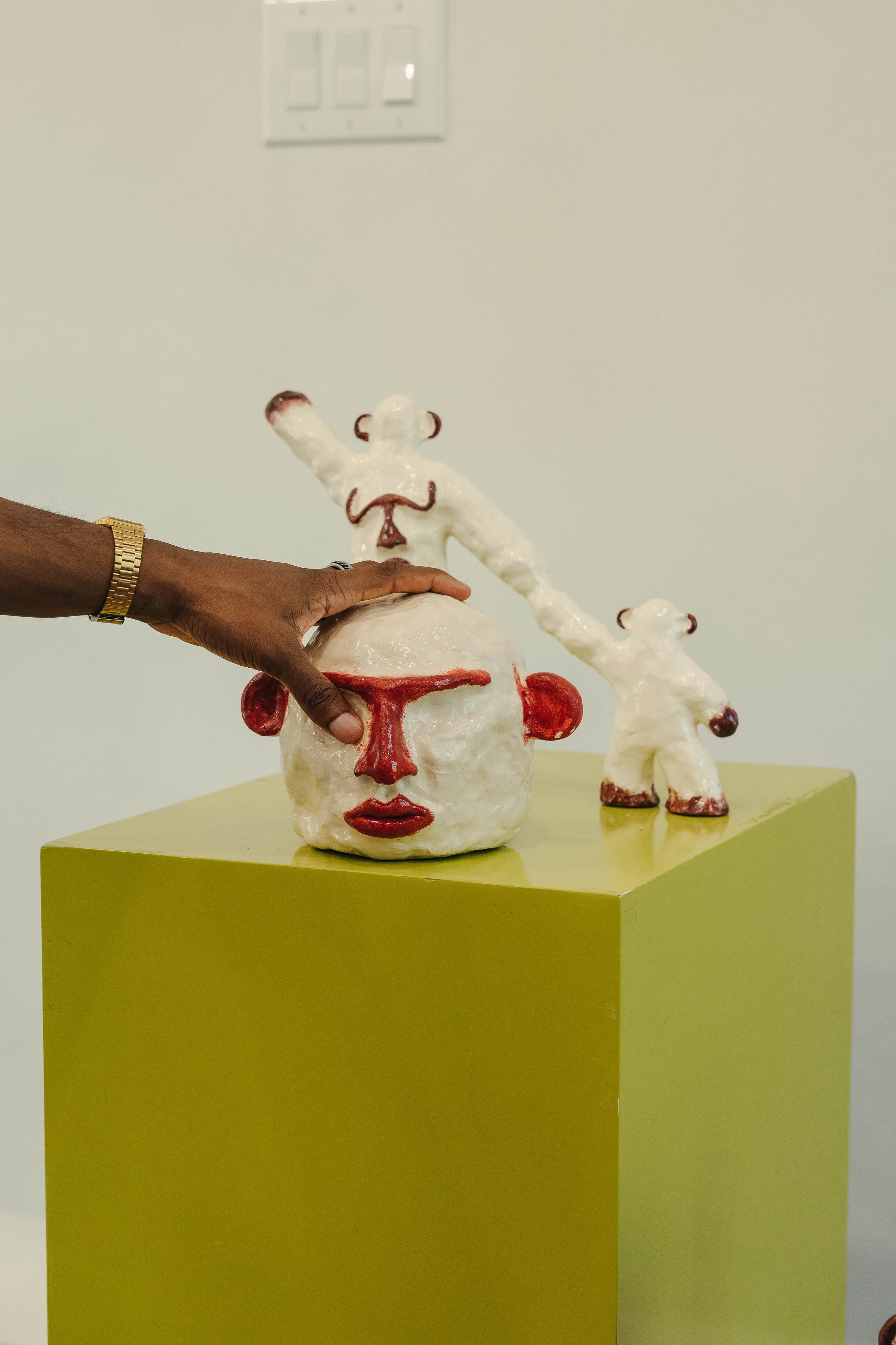 Hand-molded head and connected figures displayed on a plinth